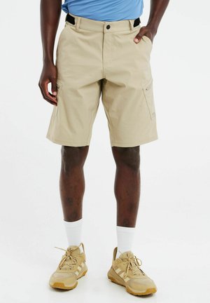 Beige cargoshorts met een casual pasvorm, voorzien van zijzakken, een gladde textuur en een verstelbare taille, gecombineerd met tan-sportschoenen en witte sokken.