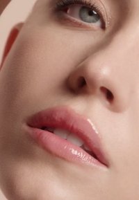 Primer plano de un rostro con piel suave y clara; labios llenos y brillantes en un rosa pálido; y ojos azules brillantes con un maquillaje sutil.