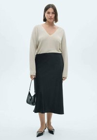 Beige gebreid sweater met een V-hals, gecombineerd met een zwarte midi rok. Zwarte puntige ballerina's en een kleine zwarte handtas maken de outfit compleet.