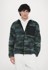 Fleece jacket featuring a multicolor abstract pattern in green and black, with a front zip and a black chest pocket. Textured fabric.