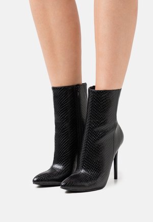 Botines negros de tobillo hechos de un material texturizado y brillante, con punta afilada y tacón de aguja, presentando un detalle de cremallera lateral.