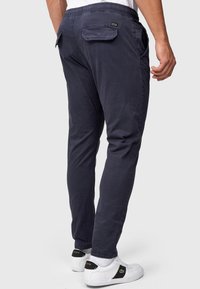Navy blue, tapered pants with a soft texture, elastic waistband, and two rear pockets. Paired with white sneakers featuring black accents.