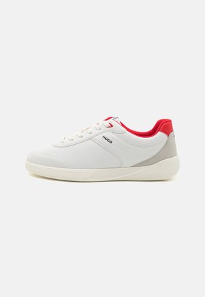 White sneaker with a textured finish, red accents on the tongue and heel, and a gray side panel. Features a cushioned sole and lace-up design.