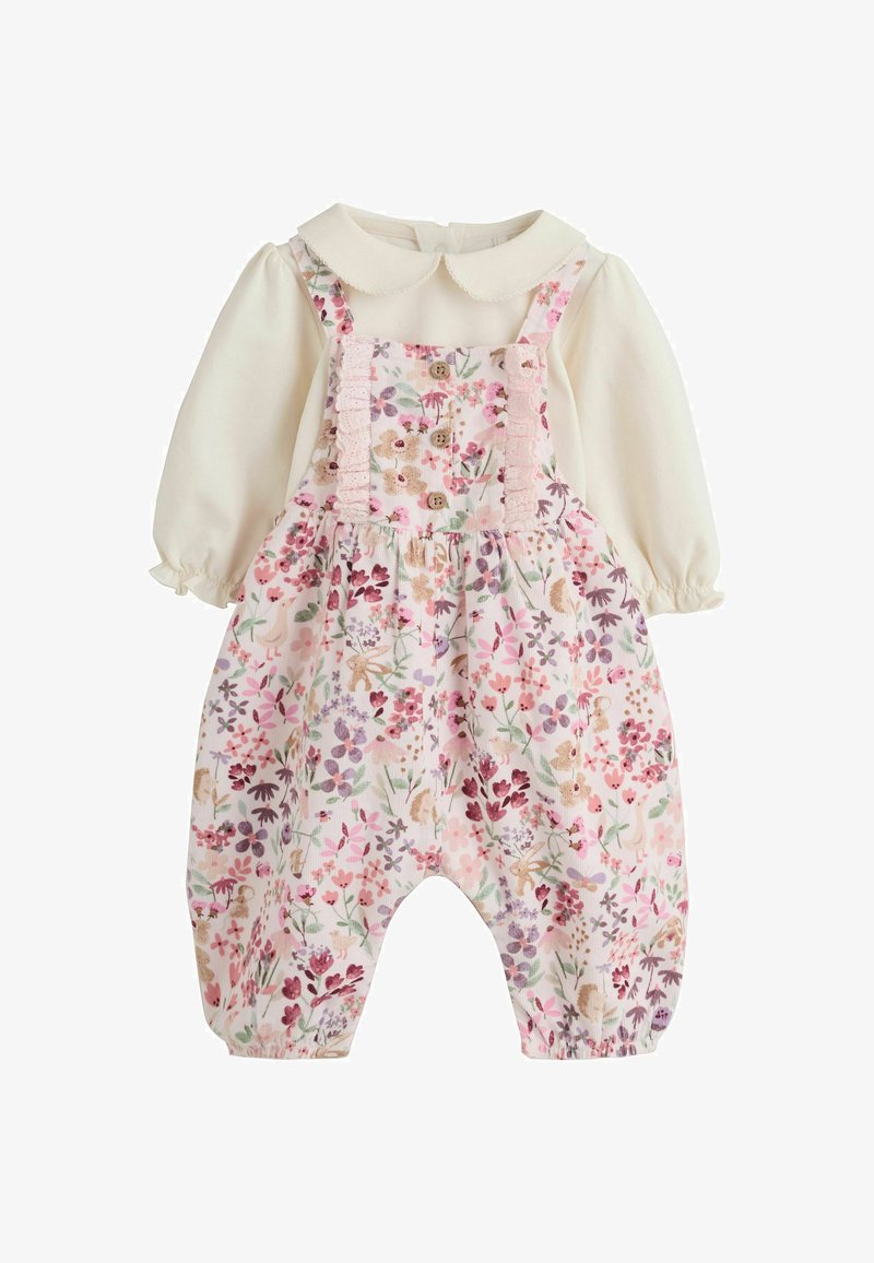 T-shirt bébé crème à manches longues avec col Claudine sous une salopette rose à motifs floraux avec boutons et volants sur les bretelles.