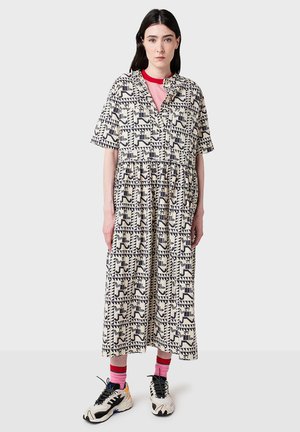Donna che indossa un abito midi a fantasia con forme geometriche in bianco e nero, una maglietta rosa a girocollo, calze rosa e sneakers in bianco e nero.