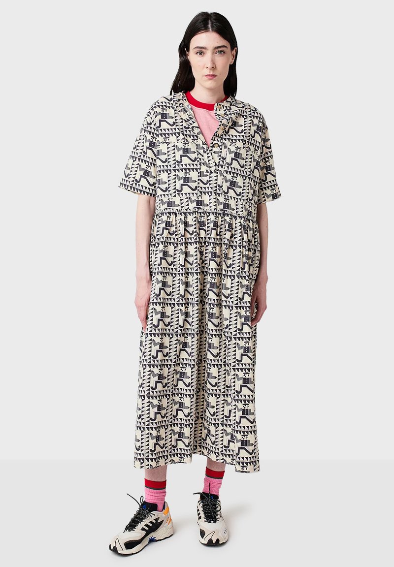 Donna che indossa un abito midi a fantasia con forme geometriche in bianco e nero, una maglietta rosa a girocollo, calze rosa e sneakers in bianco e nero.
