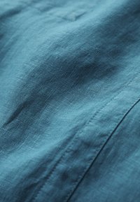 Tela de color teal con textura, de superficie lisa y ligeramente arrugada. Los detalles de costura visibles realzan el diseño de la tela.