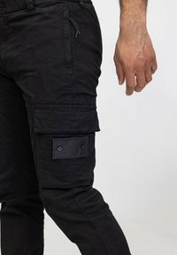 Pantalons cargo noirs en tissu durable, dotés de multiples poches, d'une coupe ajustée, de détails de poches à rabat boutonnées et de coutures renforcées.