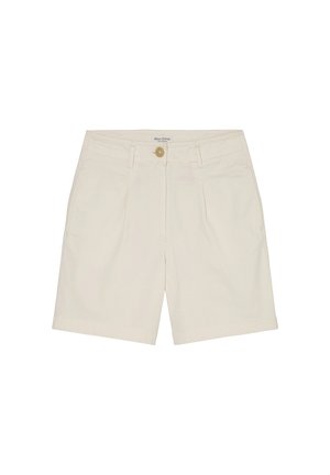 Persoon draagt een groene korte mouwen trui, beige knielange shorts, zwarte sandalen met gesp, staand tegen een effen witte muur.