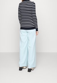 Granatowo-biały sweter w paski z dzianiny połączony z jasnoniebieskimi spodniami o szerokich nogawkach. Charakteryzuje się prążkowaną strukturą i dopasowanymi ściągaczami przy mankietach. Czarne buty na blokowym obcasie.