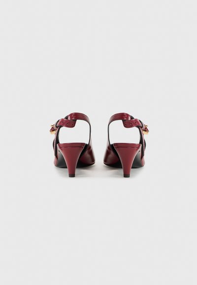 Burgundy leather heels with a pointed toe, curved cut-out sides, and an adjustable ankle strap featuring gold-tone hardware.