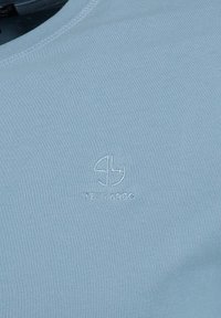 T-shirt en coton bleu clair avec un col rond et une texture côtelée subtile ; il présente un logo brodé "Key Largo" sur la poitrine gauche.