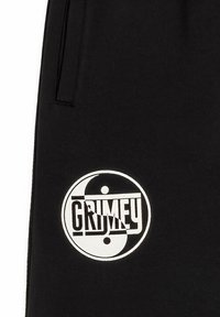 Zwarte joggingbroek met een cirkelvormige witte graphic met de tekst "GRIMEY" en een yin-yang ontwerp. Het materiaal lijkt zacht met een gladde textuur.