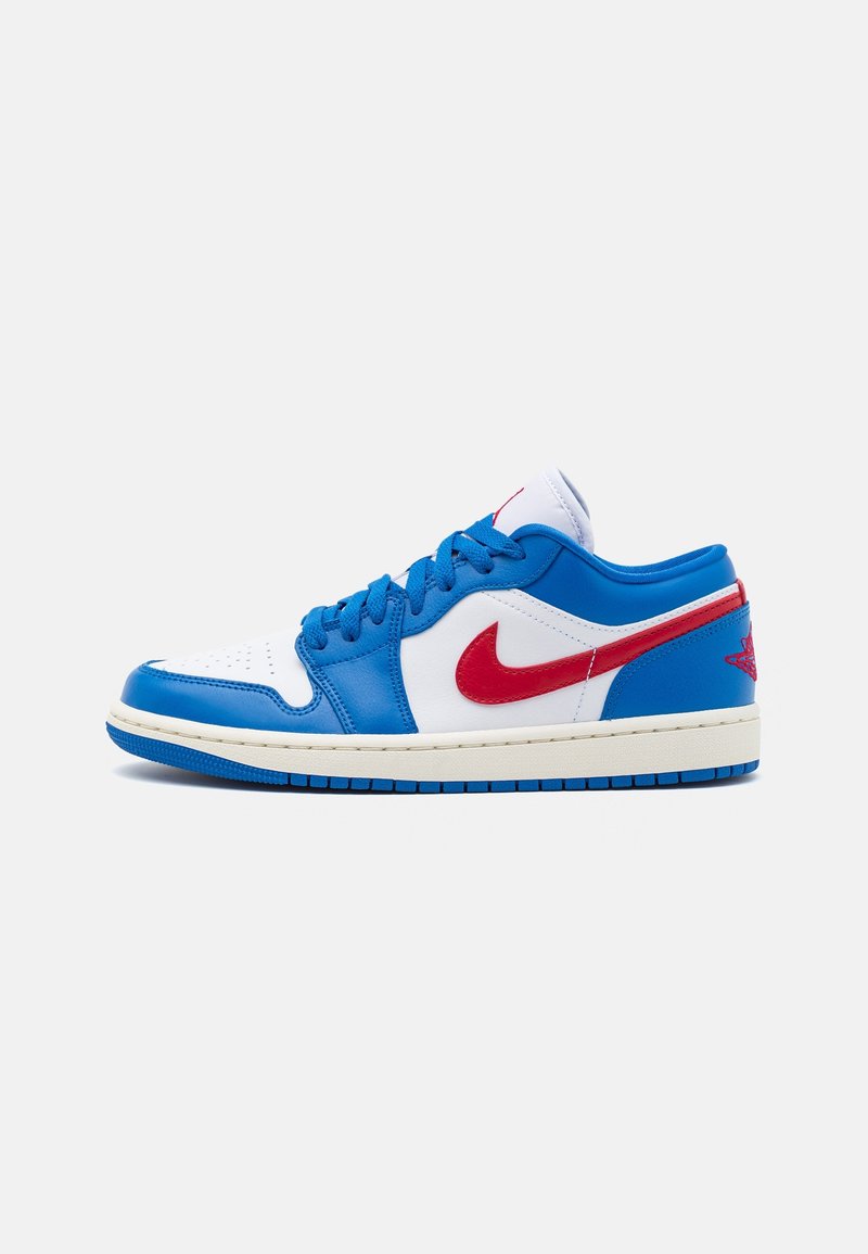 Baskets basses avec base blanche, surpiqûres bleues, lacets bleus, logo Nike rouge, logo rouge au talon et semelle intermédiaire blanche avec semelle extérieure bleue.