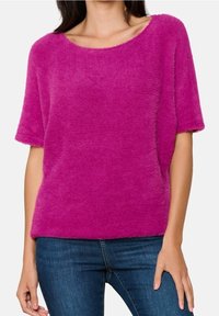 Luddig rosa kortärmad tröja med vid halsringning och avslappnad passform, bärs med blå jeans. Strukturerad yta med synliga ränder.