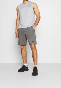 Grå ärmlös sporttröja och grå shorts, båda med Nike-logotypen, kombinerat med svarta sneakers och vita strumpor med accenter.