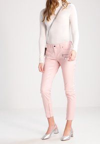 Pantalones de cuero sintético de color rosa claro con un diseño ajustado, bolsillos con cremallera y cremalleras en los tobillos, combinados con zapatos de tacón bloque plateados.