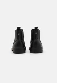 Bottes de cheville en cuir noir avec une texture lisse, des panneaux élastiques sur les côtés, une pointe ronde et une semelle en caoutchouc à motif. Tirant arrière pour un enfilage facile.
