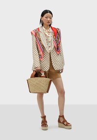 Beige polka-dot blazer with an oversized red and brown silk scarf, brown shorts, and a straw handbag with leather accents and wedge sandals.