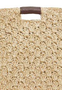 Vævet naturlig stråtaske med en struktureret cremelook, der har et brunt læderhåndtag og et indviklet mønster af sammenflettede fibre.