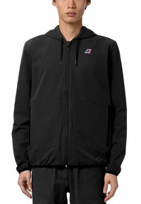 Giacca nera con zip e cappuccio, realizzata in tessuto morbido. Presenta due tasche frontali e un piccolo logo in accentuazione sul lato sinistro del petto.