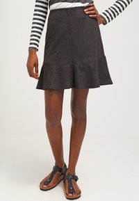 Jupe courte en suédine noire avec un ourlet évasé, présentant une texture douce. Associée à des sandales plates noires. Haut à rayures horizontales à manches longues.