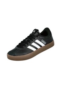 Zapato deportivo negro con diseño de tres rayas blancas, hecho de material similar al cuero, con suela de goma marrón y cordones negros.