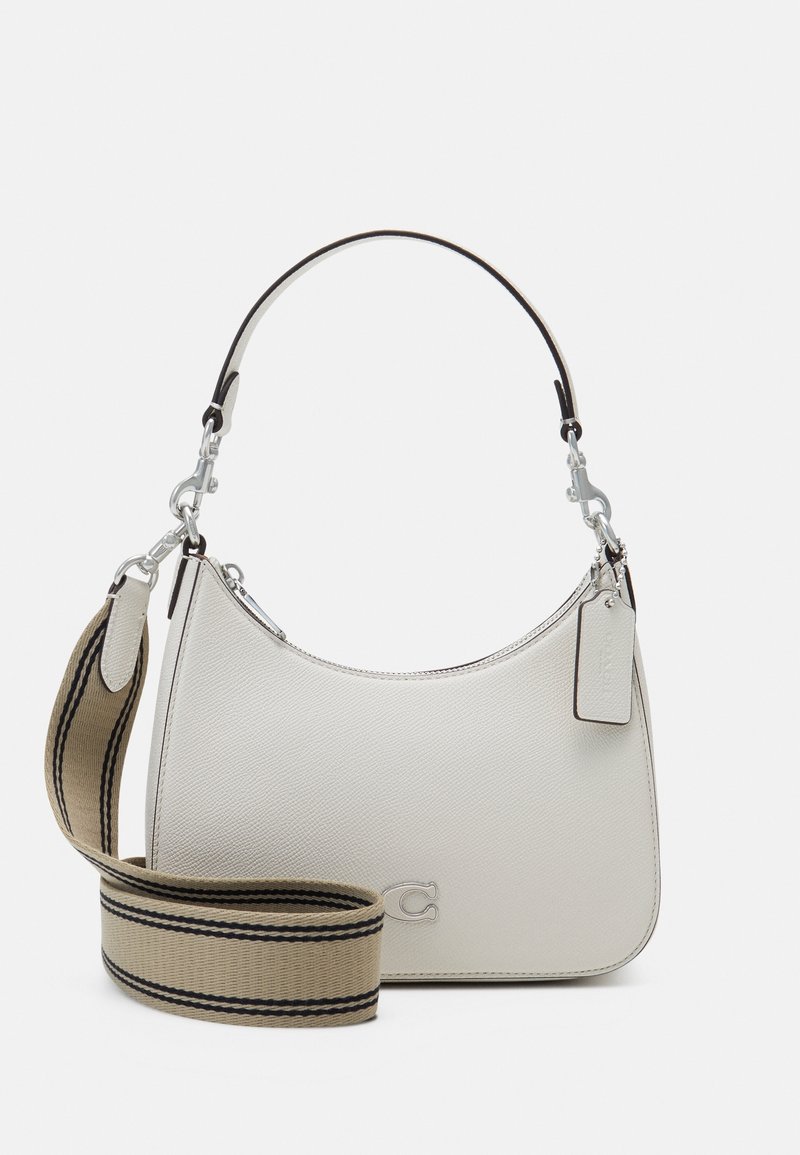Sac à main en cuir blanc avec une quincaillerie argentée, une sangle courte et une sangle d’épaule en tissu beige plus large avec des rayures noires.