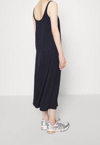 Granatowa sukienka bez rękawów o luźnym kroju i okrągłym dekolcie, zestawiona z srebrno-pomarańczowymi butami do biegania. Gładki, lekki materiał.