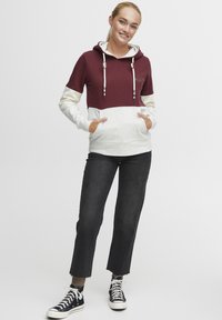 Maroon og hvit fargeblokkerte hettegensere med snorhette, ribbede mansjetter og frontlommer. Kombinert med svarte avkortede jeans og joggesko.