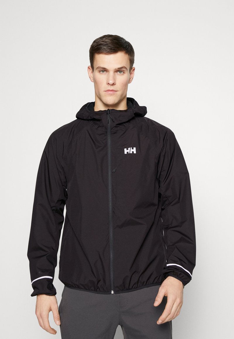 Schwarze wasserdichte Jacke mit Kapuze, ausgestattet mit einem Frontreißverschluss, elastischen Bündchen und einem reflektierenden Streifen an den Ärmeln. Logo auf der Brust.