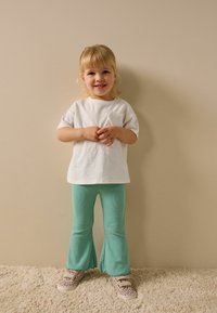 Fehér, rövid ujjú póló szíves zsebbel, mentazöld bordázott, bővülő nadrággal és bézs, leopárdmintás tornacipővel párosítva.