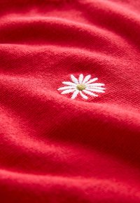 Red knitted fabric featuring white embroidered daisy with a green center, showcasing softness and texture with visible stitching detail.