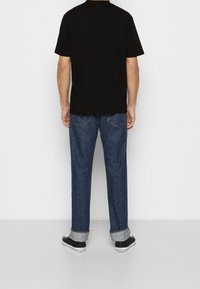 Camiseta negra de manga corta con corte recto, combinada con vaqueros de denim azul oscuro, con puños enrollados y zapatillas negras.