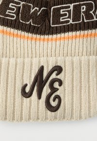 Kootud müts kreemjas toonis, pruunide ja oranžide triipudega. Disainil on tikkimiga "NE" logo ja sooniline tekstuur.