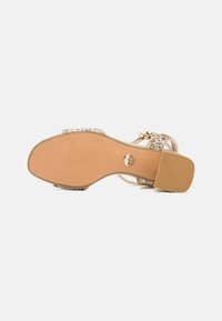 Beige klacksandaler med en texturerad sula och glittrande detaljer på remmarna. Har en justerbar spänne för en säker passform.