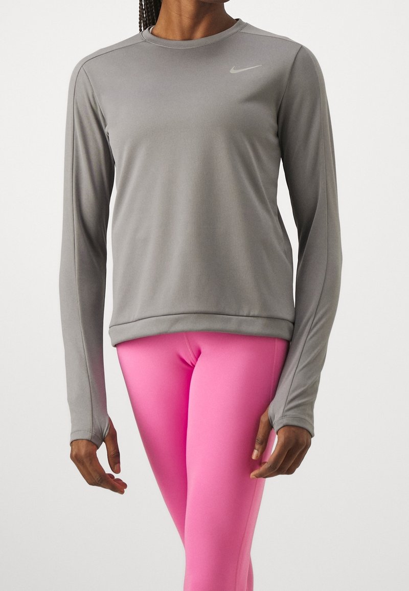 T-shirt de sport à manches longues gris clair avec un col rond et une coupe ajustée, associé à des leggings rose vif. Présente un logo discret sur la poitrine.