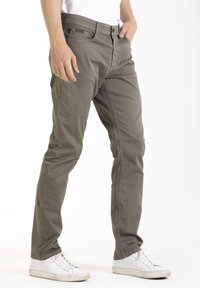Chino en coton gris clair avec une coupe droite, des poches avant et un discret logo sur la ceinture. Associé à des baskets blanches.