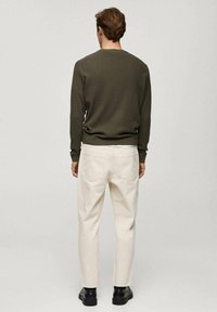 Olivgrüner gerippter Pullover und hellbeige gerade geschnittene Hose. Die Hose hat zwei Gesäßtaschen; die Schuhe sind schwarz und haben ein glattes Finish.