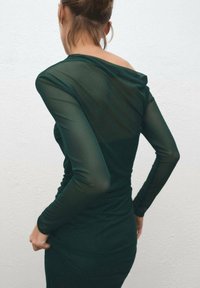 Rochie cu mâneci lungi, de culoare verde închis, cu spate și mâneci transparente, design ajustat și decolteu drapat. Textură netedă și material ușor.
