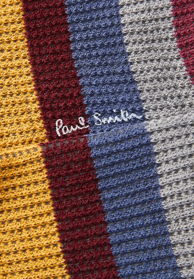 Stickad tyg med djärva vertikala ränder i gul, vinröd, blå, grå och vit, med handskriven "Paul Smith"-logotyp.