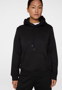 Felpa nera con cappuccio realizzata in un tessuto misto cotone. Presenta una tasca frontale, cappuccio con lacci e polsini a coste. Design minimalista senza loghi visibili.