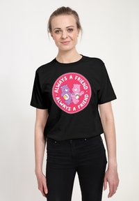 Camiseta negra con un gráfico circular sobre un fondo rosa, dos osos de dibujos animados sosteniendo corazones y el texto "Siempre un Amigo."