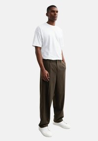 T-shirt blanc à manches courtes, coupe décontractée, associé à un pantalon ample marron foncé et des baskets blanches. Texture lisse, design minimal.