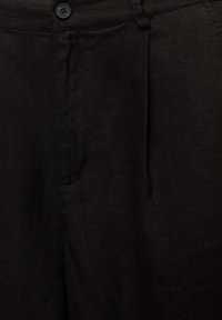 Mustat pellavahousut, joissa on teksturoitu kangas, etupleatti ja nappisuljenta. Sivutaskut tarjoavat käytännöllisyyttä.