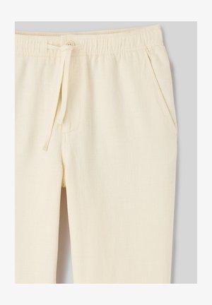 Pantalon texturé blanc cassé avec taille élastique, fermeture par bouton, cordon de serrage et poches latérales sur un fond gris clair.