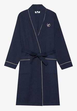 Mørkeblå badekåbe i waffle-struktur med sjalkrave, guld piping og bindebælte. Har to frontlommer og et broderet logo på brystet.