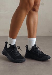 Scarpe sportive nere con suola texturizzata, dotate di lacci e colletto imbottito, abbinate a calzini bianchi a coste.