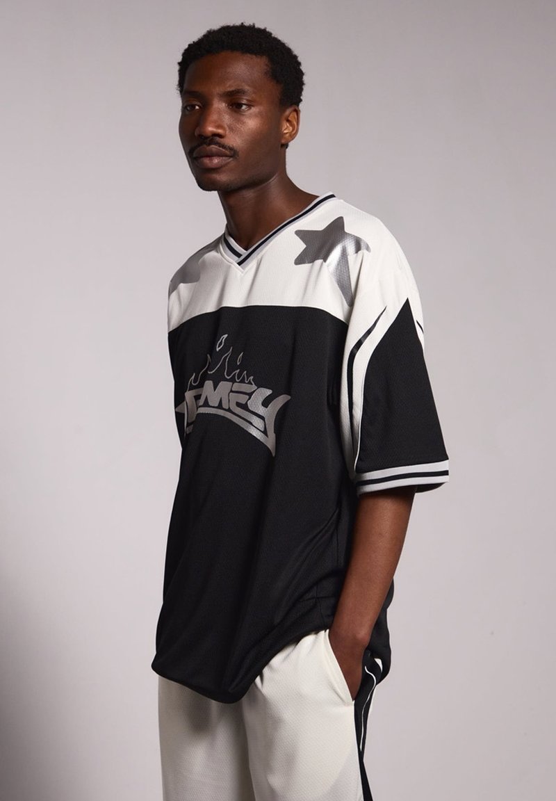 Jersey de gran tamaño en blanco y negro con acentos de estrellas, textura de malla y logo en contraste. Diseño de mangas cortas y escote en V con detalles a rayas.
