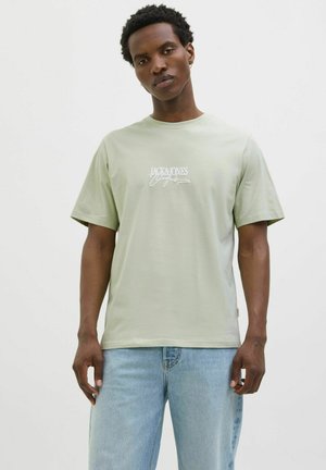 Tkako svijetlozelena majica od pamuka, s kratkim rukavima i okruglim izrezom. Na prednjoj strani se nalazi bijeli logo "JACK & JONES" napisan kucanim pismom.